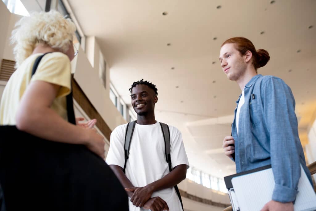 Photo représentant 2 étudiants et une étudiante en train de discuter au sein d'un établissement scolaire.
