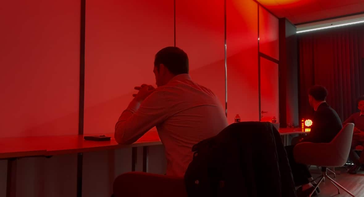 Un recruteur dans une salle à l'ambiance tamisée rouge, concentré, en train d'écouter un candidat pitcher