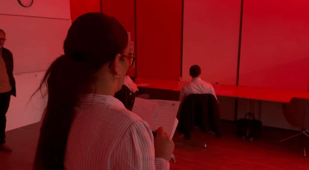 Une candidate, avec des feuilles, en train de lire son pitch. Les recruteurs lui tournent le dos