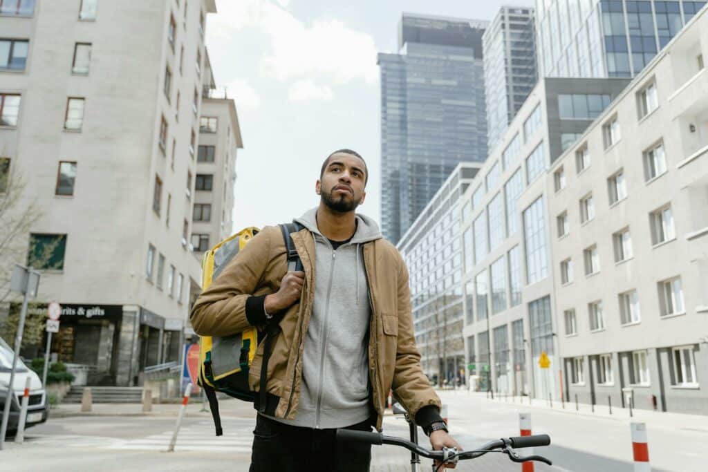 Homme avec un sac de livraison sur le dos, tenant un vélo en milieu urbain