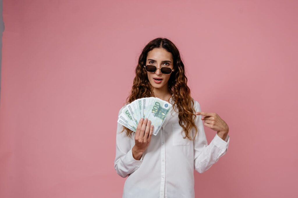Femme portant des lunettes de soleil, tenant des billets d'euros, sur un fond rose